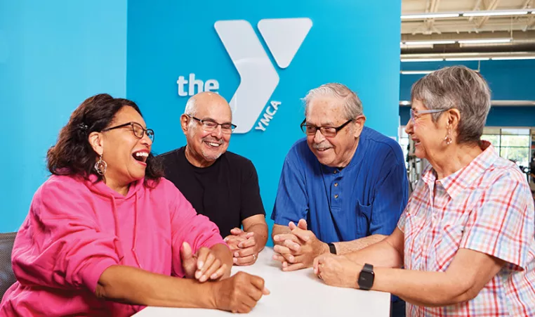 Group of adults laughing with the YMCA logo behind them